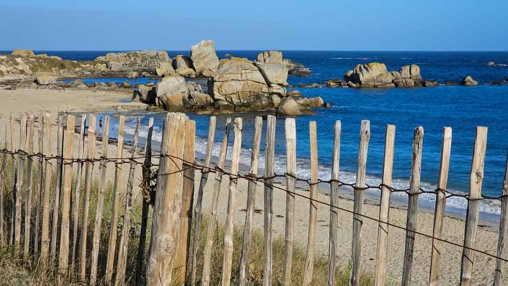 Stand-und-Meer-bei-Meneham Bretagne Frankreich Zaun im Vordergrund, Felsen und Meer im Hintergrund